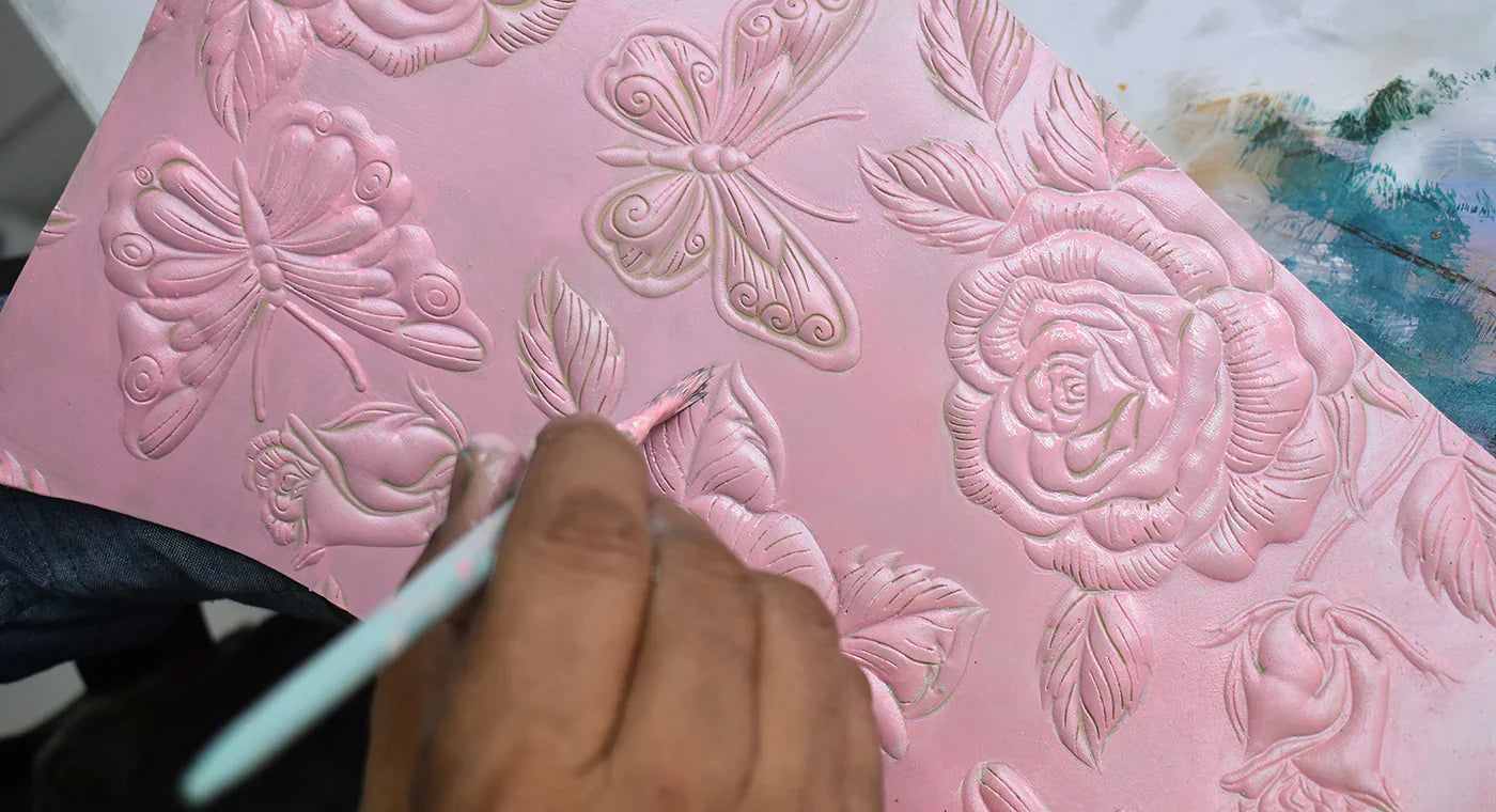 Hand holding a brush painting a pink surface embossed with floral and butterfly designs.