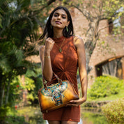 A woman posing with an Anuschka Wide Organizer Satchel - 695 featuring hand-painted elephant artwork, standing outdoors.