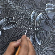 A person hand painting a dragonfly on an Anuschka Large Zip Top Tote - 698.