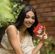 Woman smiling outdoors and showing a small leather credit card case with hand-painted floral artwork by Anuschka.