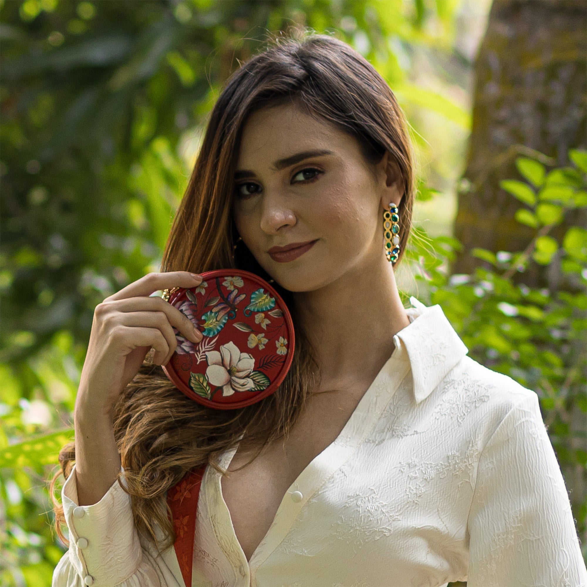 A woman holding a Round Coin Purse - 1175 by Anuschka in a garden setting.