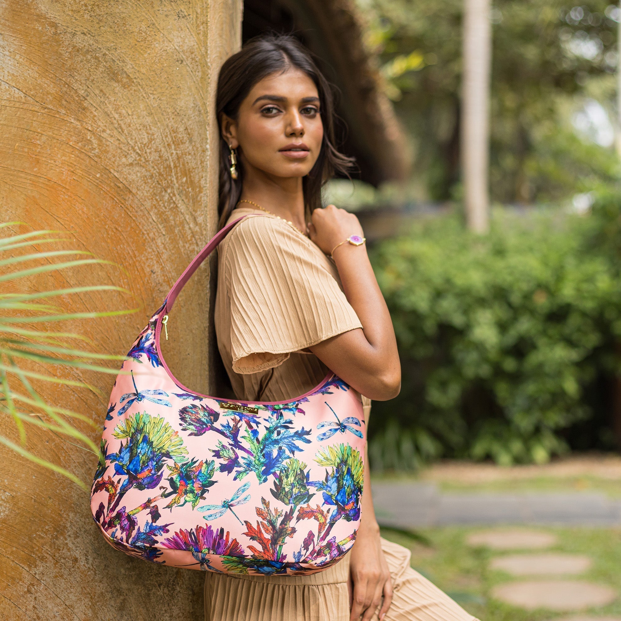 A woman in a beige outfit posing with an Anuschka Fabric with Leather Trim Large Sling Hobo - 12010, featuring zippered pockets.