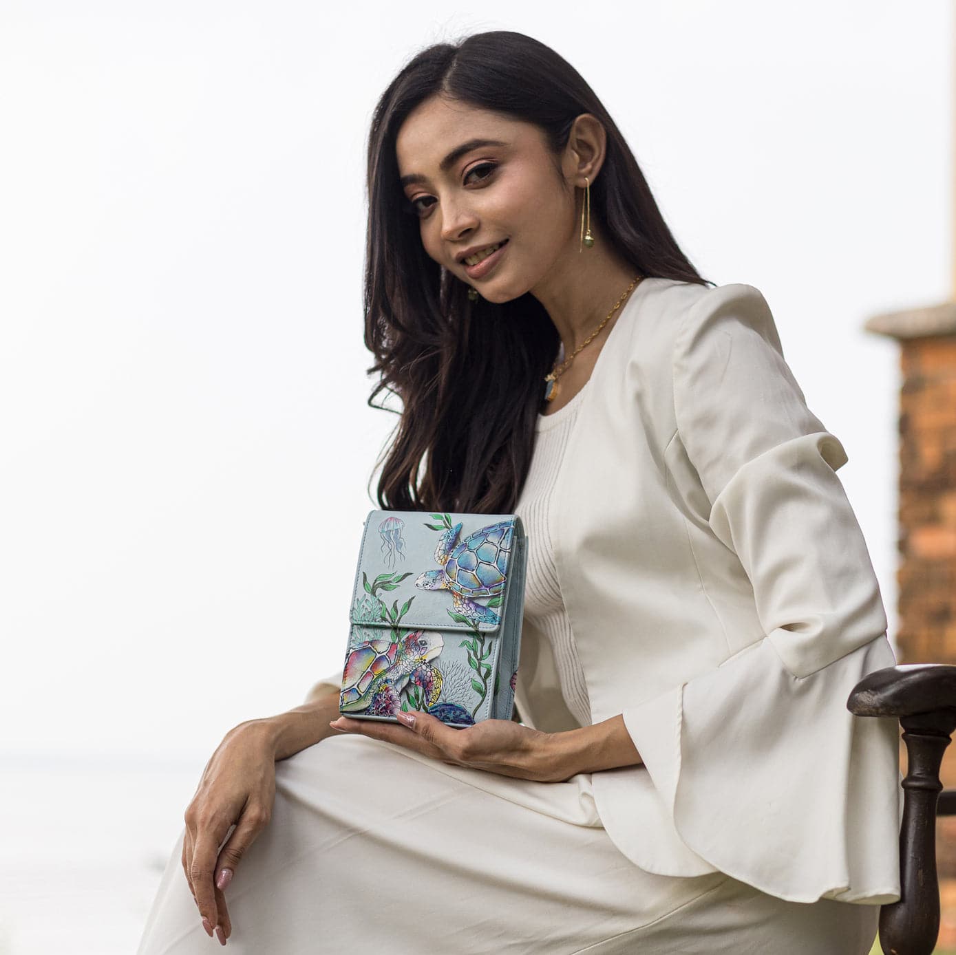 Woman in a white outfit sitting and holding an Anuschka Triple Compartment Crossbody Organizer - 412.