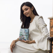 Woman in a white outfit sitting and holding an Anuschka Triple Compartment Crossbody Organizer - 412.