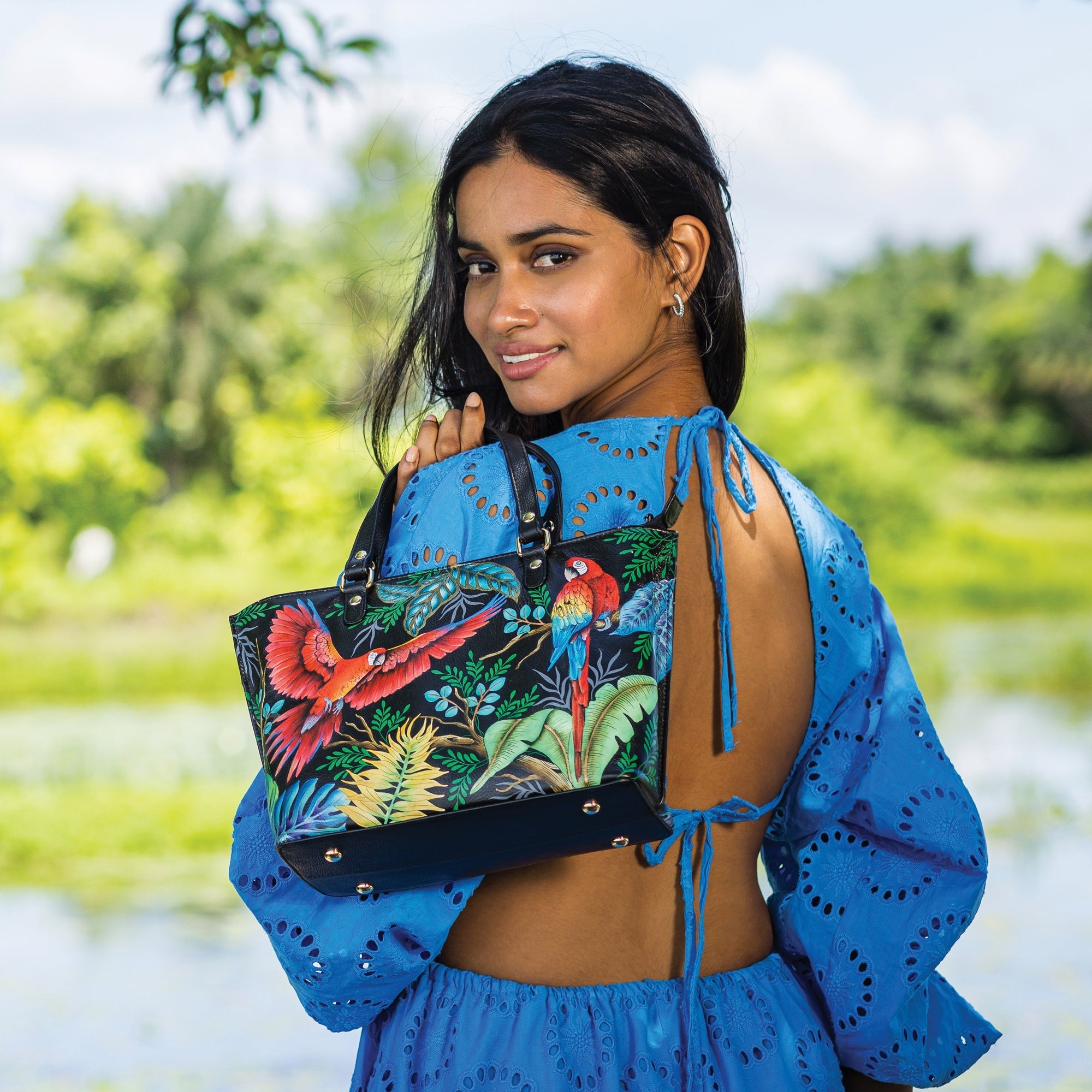 Woman holding a hand-painted, colorful Anuschka Medium Tote - 693 outdoors.