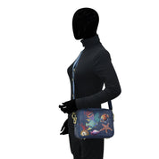 A person wearing a black bodysuit and gloves, carrying an Anuschka Twin Top Messenger - 704 with an adjustable strap and marine life design, standing against a white background.