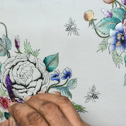 Hand painting a detailed floral design on a genuine leather Anuschka Round Coin Purse - 1175, featuring a large peony, smaller flowers, leaves, and bees.