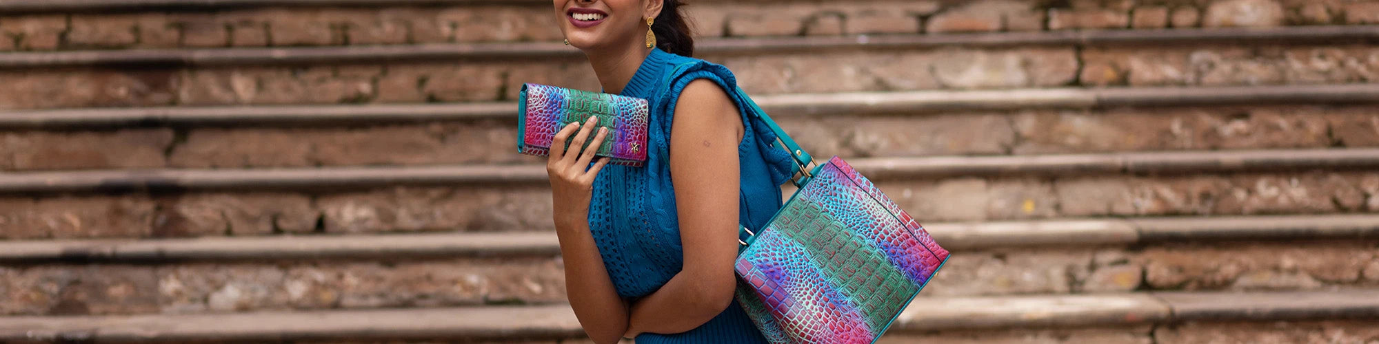 A woman in a red dress holds a multicolored floral handbag while standing near green window shutters.