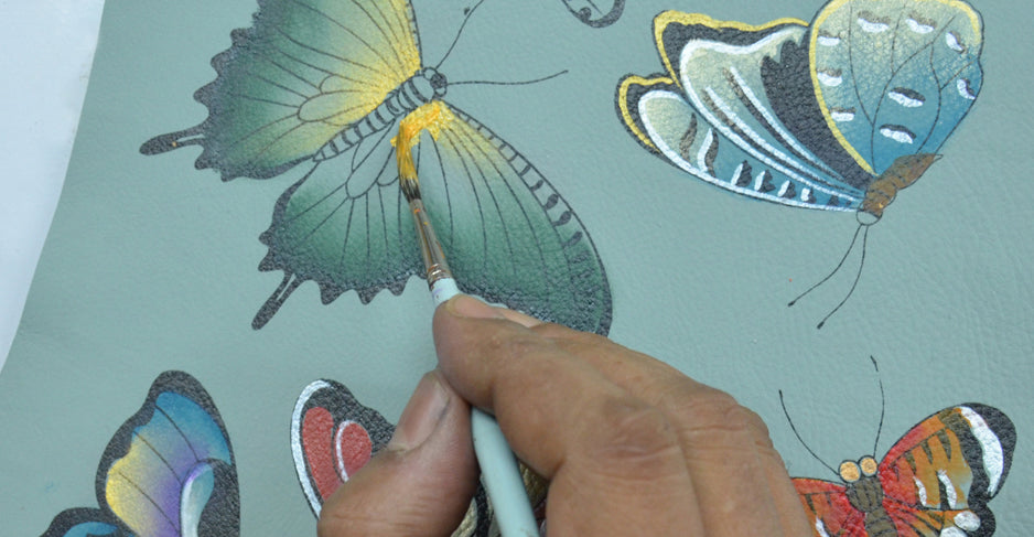 Close-up of a hand painting colorful butterflies on a blue surface using a fine brush.