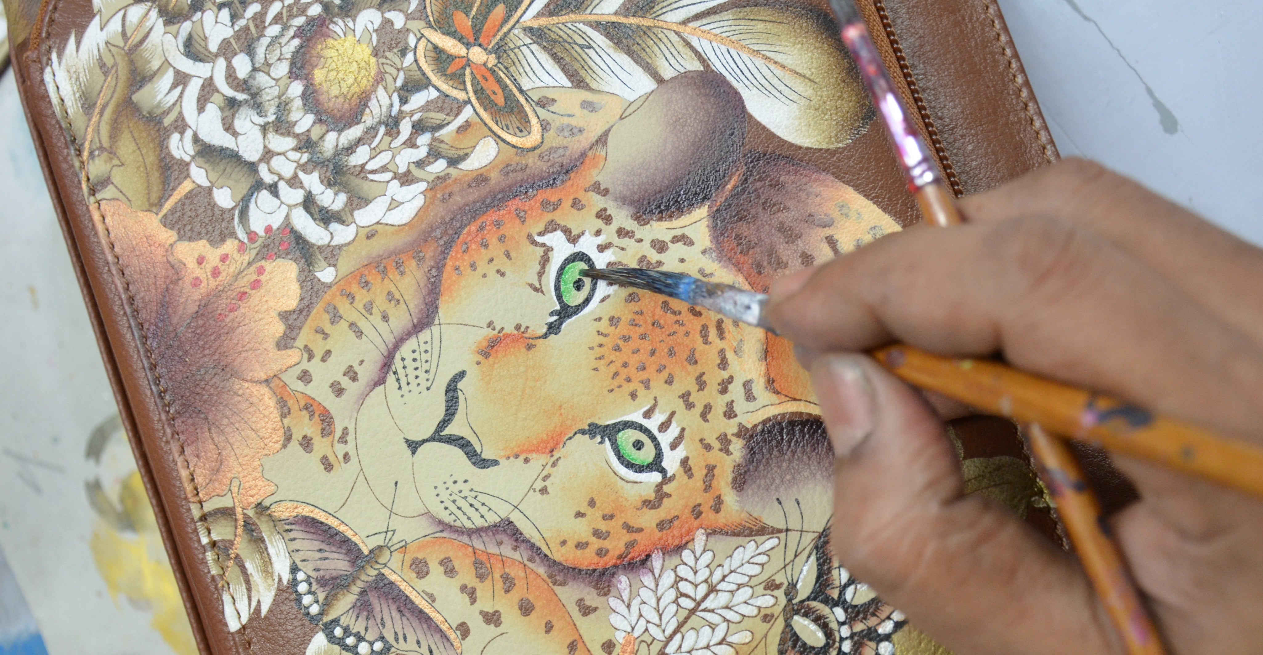 A hand is painting details on a leopard face illustration with various floral elements.