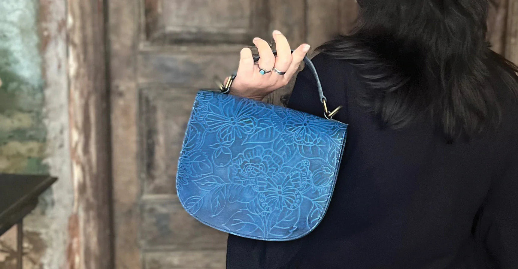 Person holding a blue floral-patterned handbag over their shoulder, standing in front of a wooden door.