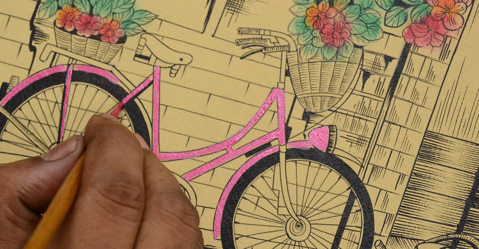 A person colors a drawing of a vintage bicycle with flower baskets, using shades of pink and green.