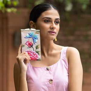 A woman in a pink dress holding a decorated **Anuschka Double Eyeglass Case - 1009** close to her face, intrigued by the art etched on its surface.