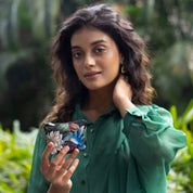 Woman holding a smartphone with an Anuschka hand-painted floral coin pouch in a garden setting.