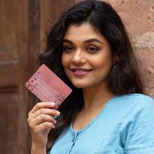 Load image into Gallery viewer, Woman holding a Anuschka Credit Card Case - 1032 made of genuine leather with card slots while smiling at the camera.
