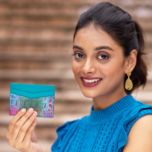 Woman holding a Anuschka Credit Card Case - 1032 with hand-painted artwork and smiling at the camera.