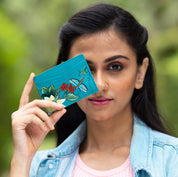 Woman holding an Anuschka leather, floral-patterned Credit Card Case - 1032 up to her face outdoors.