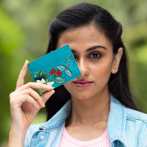Woman holding an Anuschka leather, floral-patterned Credit Card Case - 1032 up to her face outdoors.