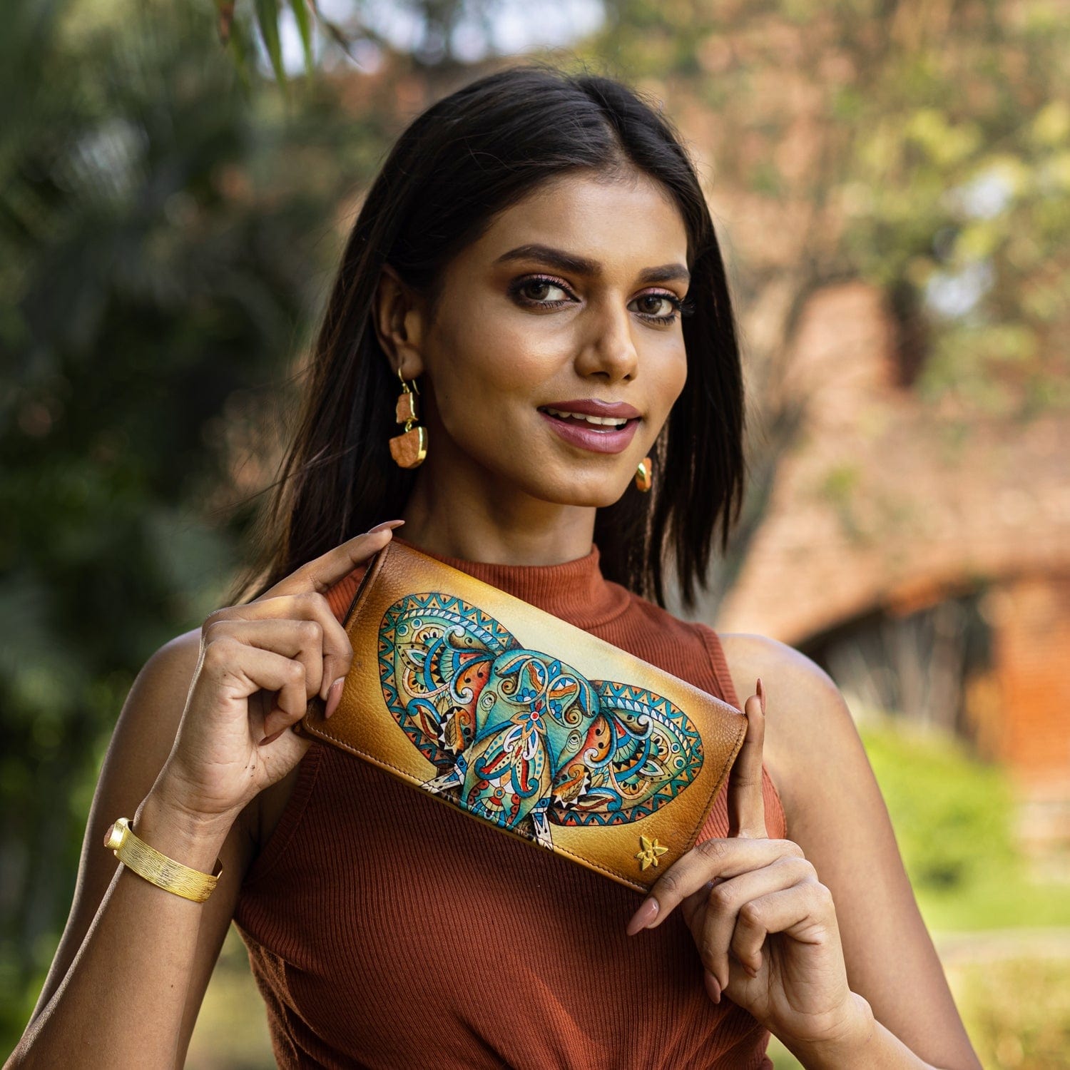 A woman holding a colorful Anuschka Accordion Flap Wallet - 1112 outdoors.