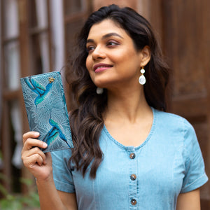 Woman holding an Anuschka Accordion Flap Wallet - 1112, bird-themed notebook and smiling.