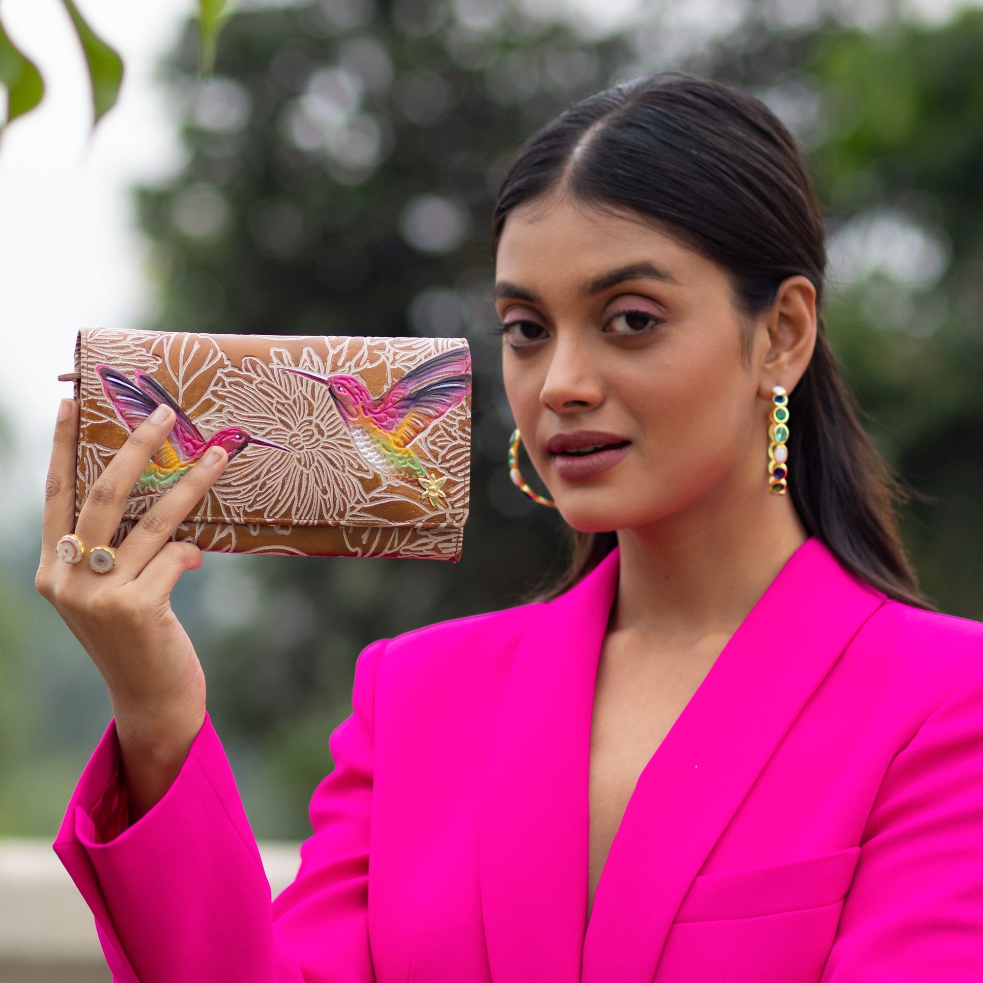 A woman in a pink blazer holding an Anuschka Accordion Flap Wallet - 1112, patterned with a butterfly design and featuring RFID protection.