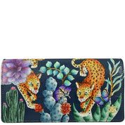 The Anuschka Accordion Flap Wallet - 1112 is a vibrant wallet adorned with hand-painted illustrations of leopards, butterflies, and various plants on a dark background. It is meticulously crafted from genuine leather and includes RFID protection.