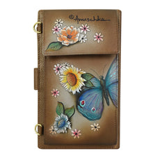 Load image into Gallery viewer, The Anuschka Cell Phone Case &amp; Wallet - 1113 is a brown leather accessory adorned with hand-painted floral and butterfly designs, showcasing sunflowers, daisies, and a large blue butterfly. The brand&#39;s signature &quot;Anuschka&quot; is prominently displayed at the top. This elegant piece also serves as a smartphone case for added functionality.
