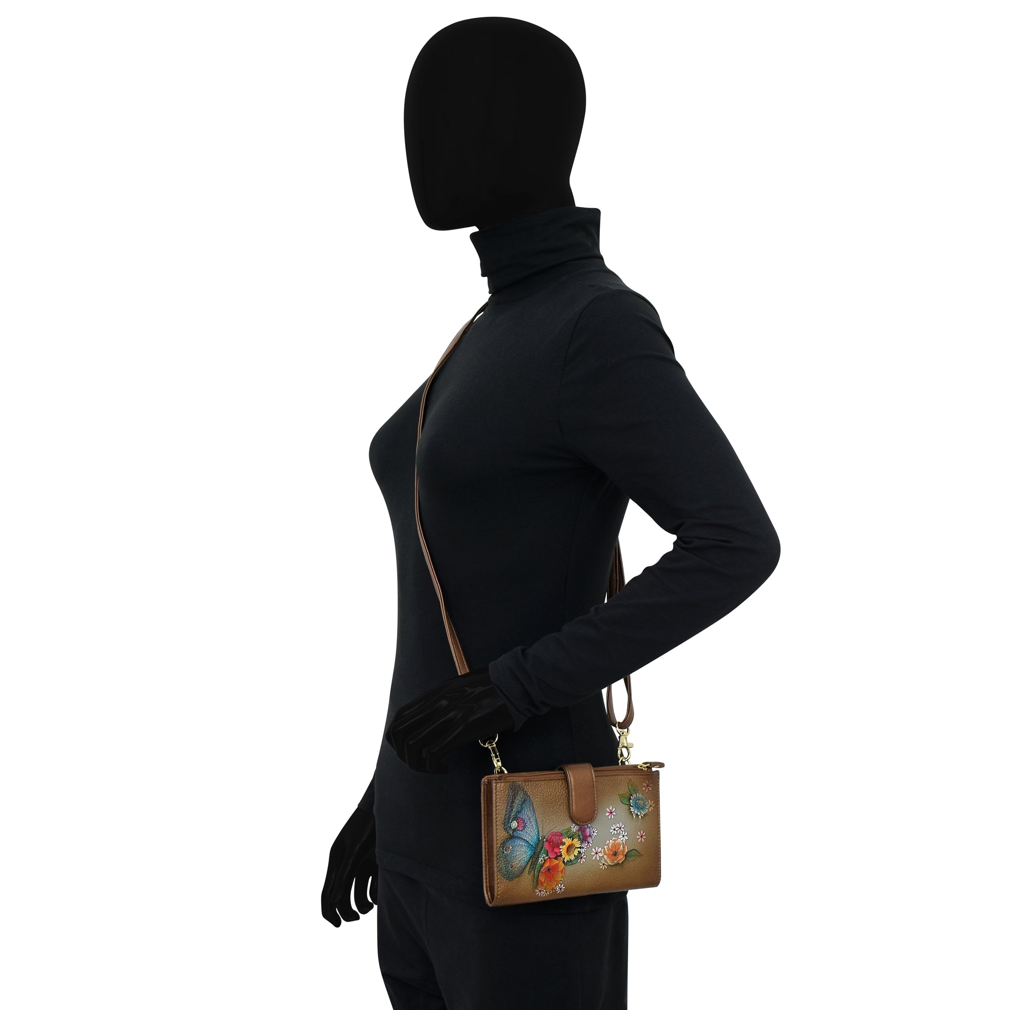 Silhouette of a person wearing a black turtleneck and holding the Anuschka Cell Phone Case & Wallet - 1113, crafted in brown leather with floral designs on the side and featuring a detachable shoulder strap.