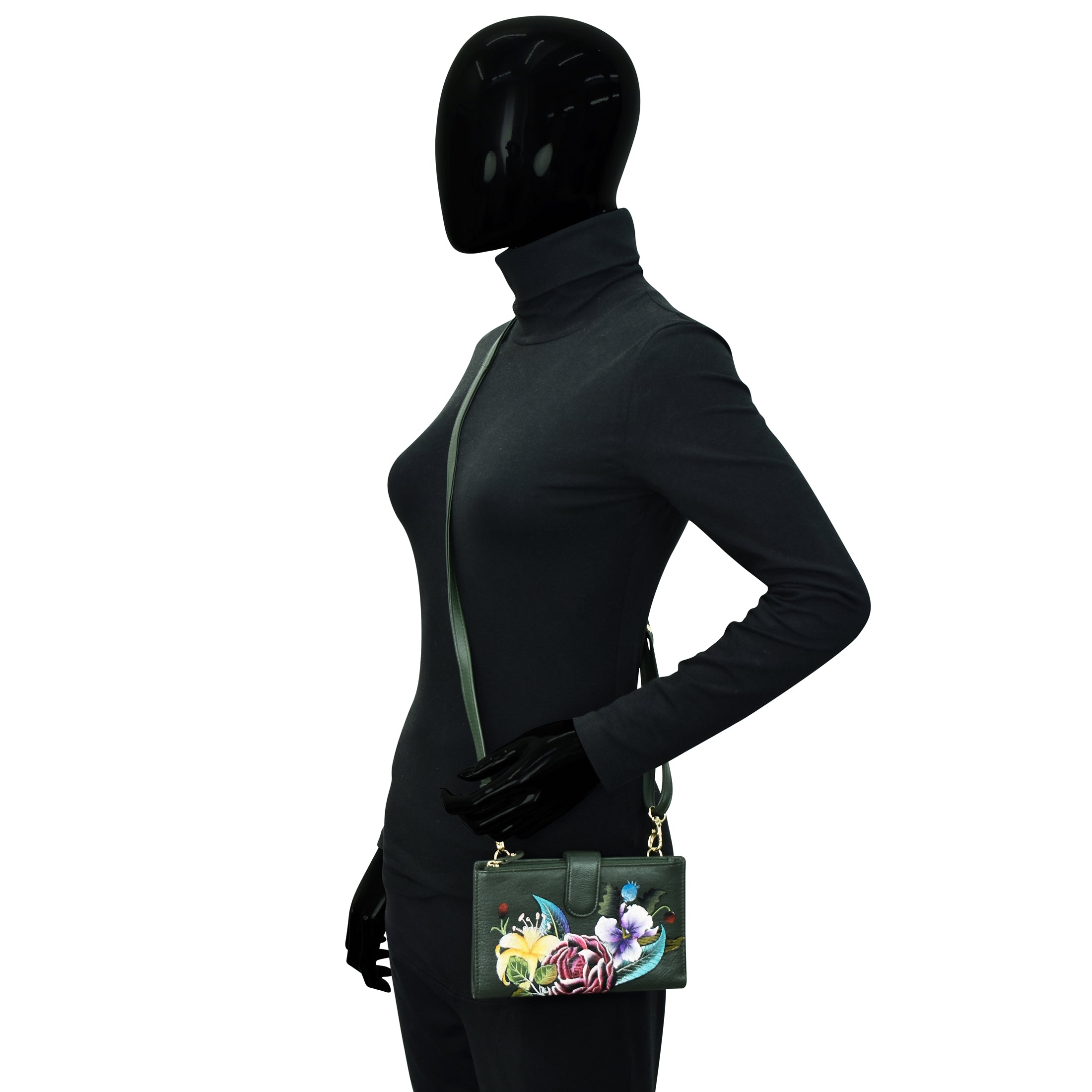 Mannequin wearing a black turtleneck bodysuit, holding an Anuschka Cell Phone Case & Wallet - 1113 with a floral design and detachable shoulder strap.