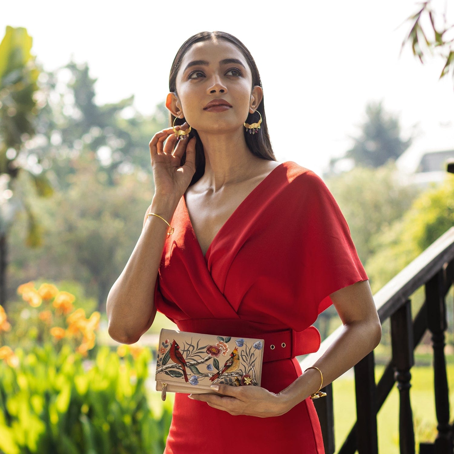 Woman in red dress holding an Anuschka Three Fold Clutch - 1136, standing outdoors.