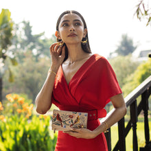 Load image into Gallery viewer, Woman in red dress holding an Anuschka Three Fold Clutch - 1136, standing outdoors.
