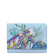 Load image into Gallery viewer, The Anuschka RFID Blocking Small Flap French Wallet - 1138 is a light blue genuine leather wallet adorned with hand-painted artwork of a colorful sea turtle and ocean plants, featuring RFID protection and a small starfish decoration on the bottom right corner.
