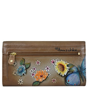 The Anuschka Triple Fold RFID Clutch Wallet - 1150 is made of genuine leather and adorned with colorful hand-painted flowers and a blue butterfly on the front. It includes a zipped pocket, offers RFID protection, and features a signature on the upper right corner.