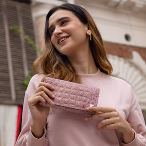 A woman in a pink sweater, smiling and holding a Three Fold Wallet - 1150 by Anuschka with RFID protected card slots.