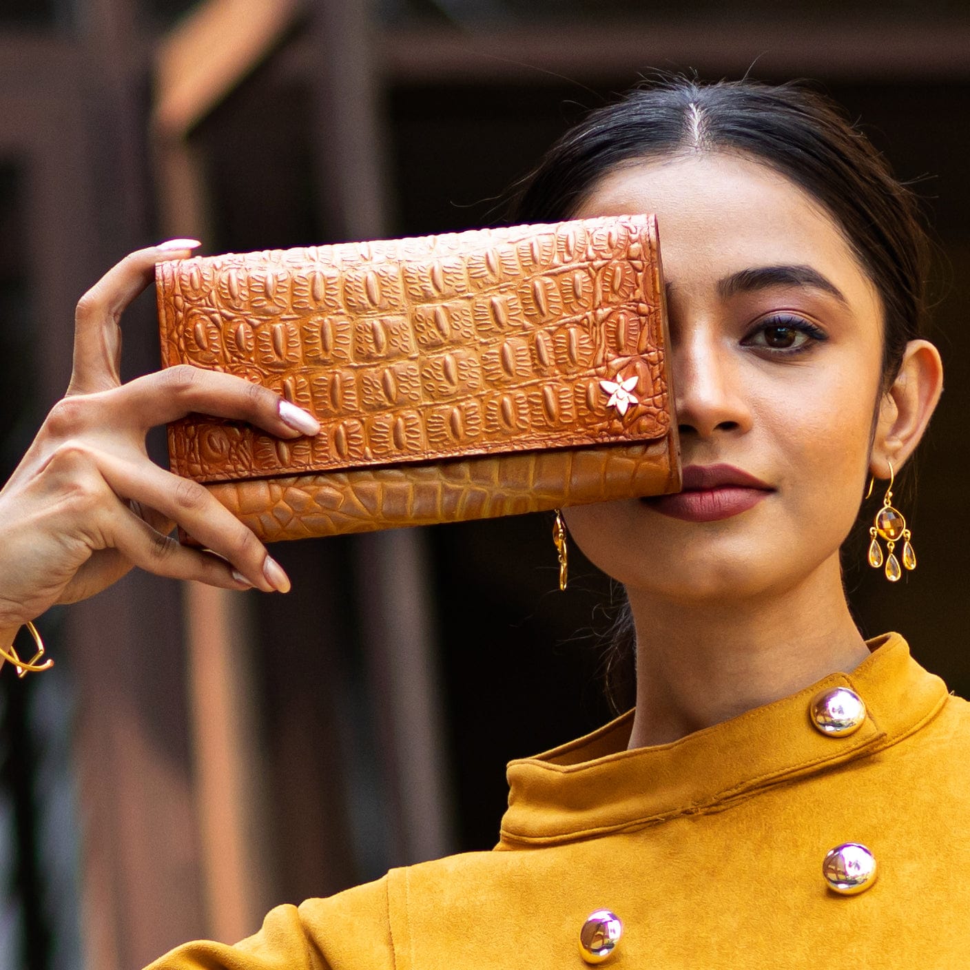 A woman holding an Anuschka Three Fold Wallet - 1150 in front of her face.