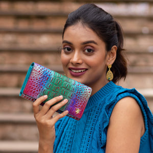 Woman holding a colorful Anuschka Three Fold Wallet - 1150 genuine leather clutch purse next to her face.