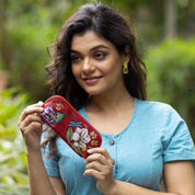 A woman holding a colorful embroidered Anuschka Medium Zip-Around Eyeglass/Cosmetic Pouch - 1163 and smiling.