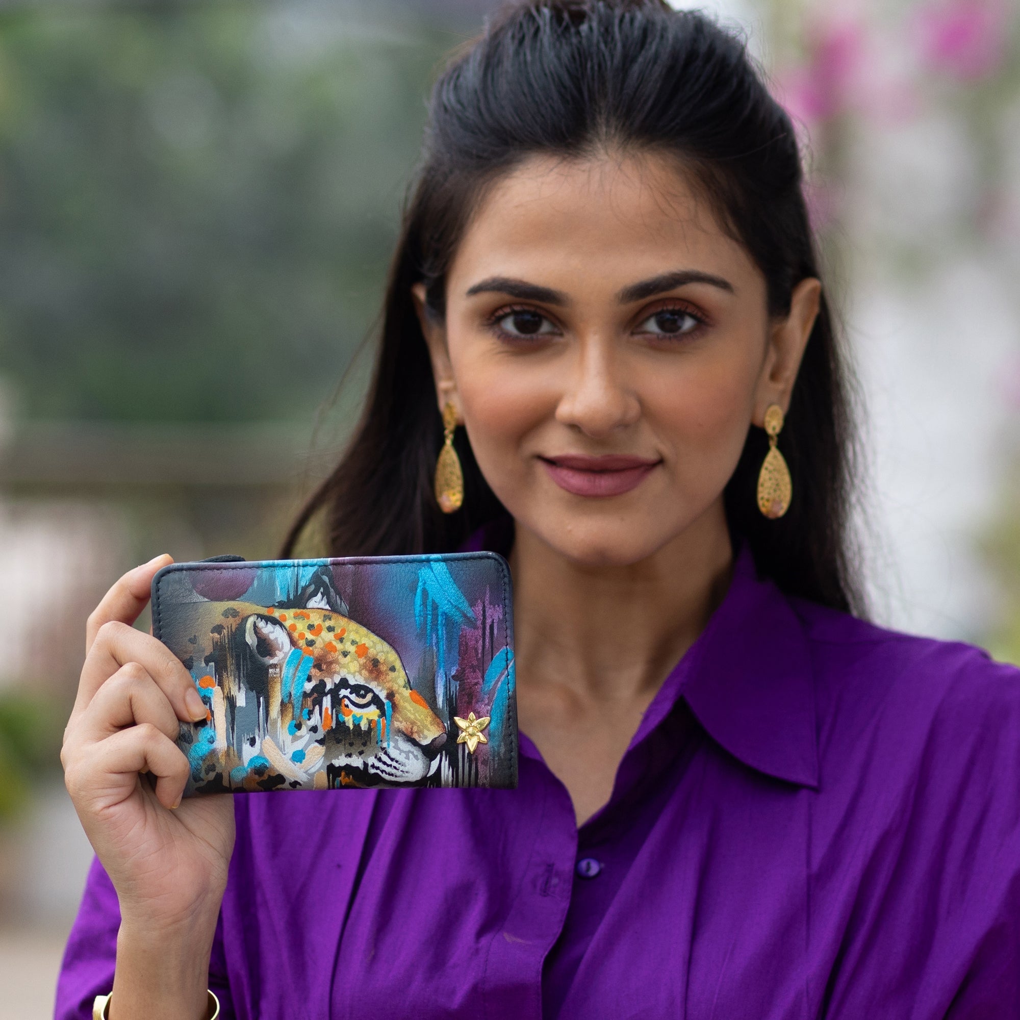 A woman holding an Anuschka Two-Fold Small Organizer Wallet - 1166 with a colorful design, smiling at the camera.