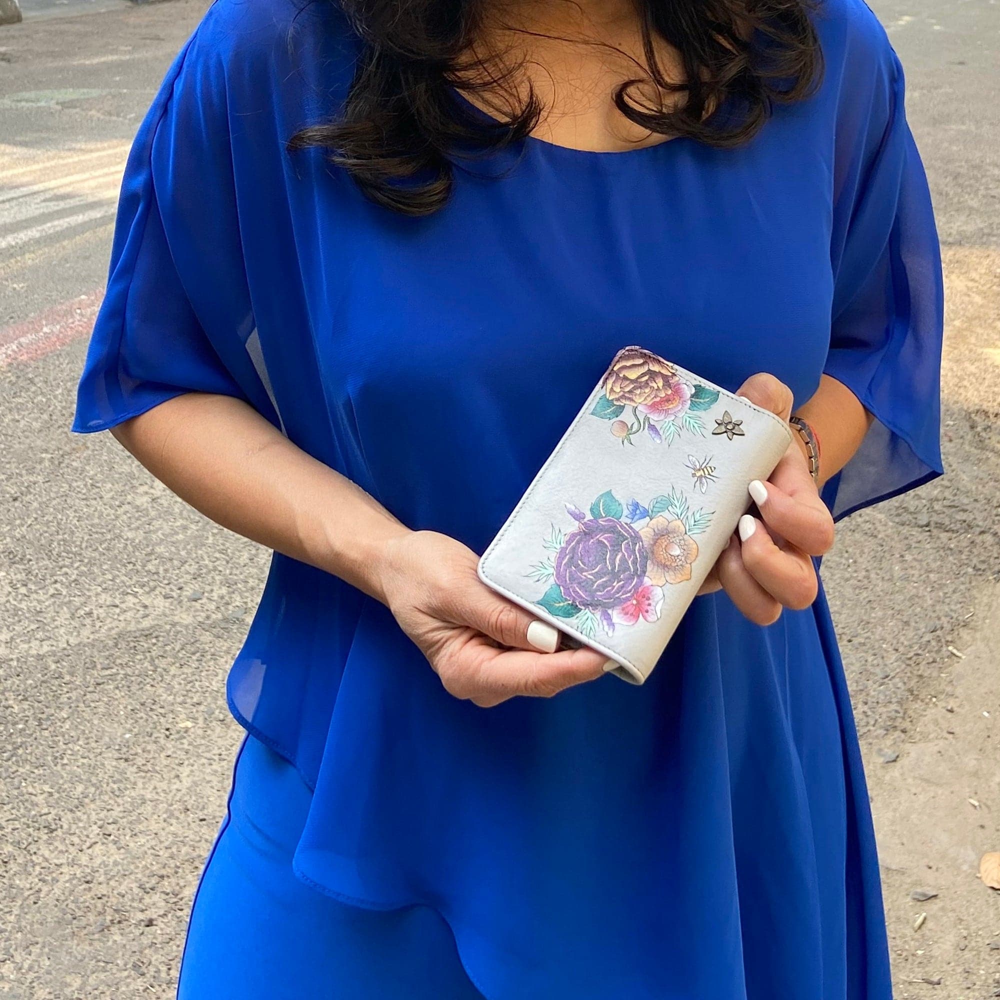 Woman in a blue dress holding an Anuschka Two-Fold Small Organizer Wallet - 1166 with RFID protection.
