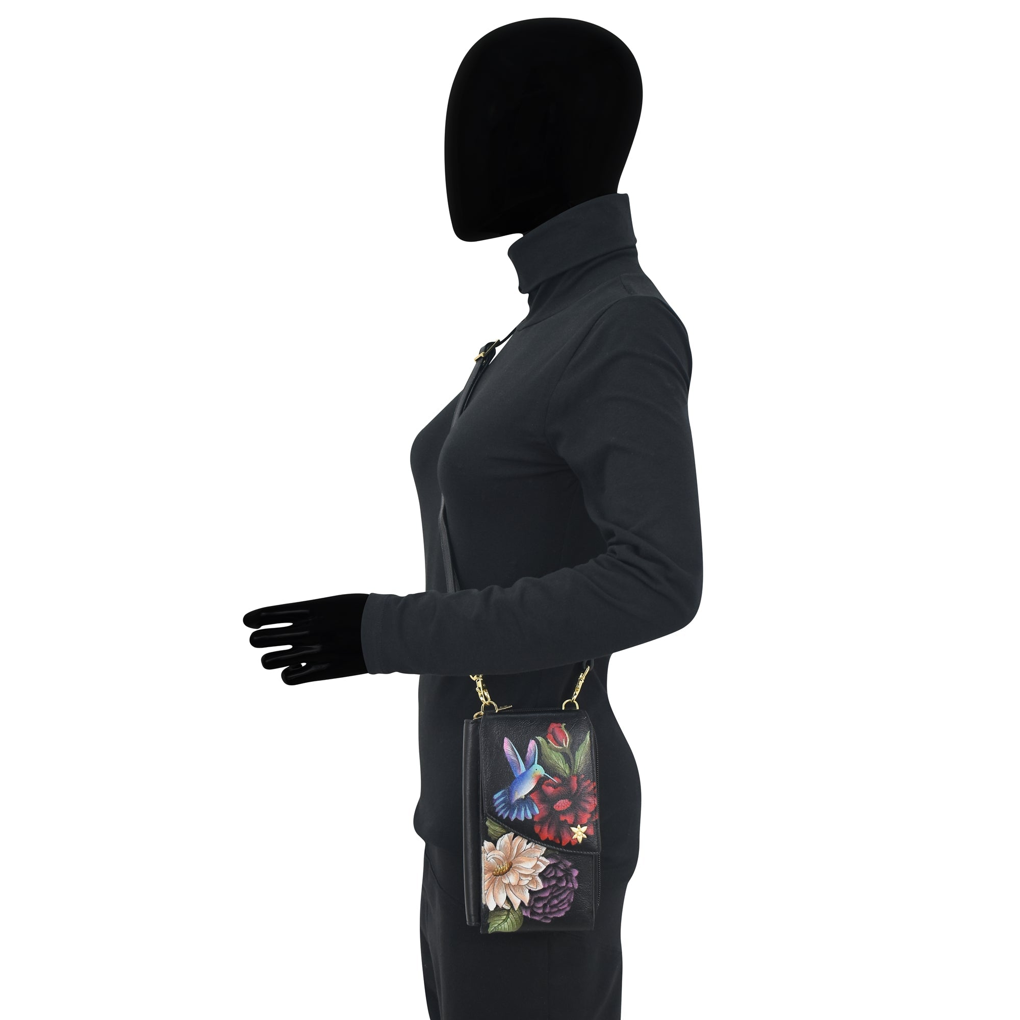 Silhouette of a person in a dark outfit holding an Anuschka Crossbody Phone Case - 1173 with a genuine leather crossbody strap by their side.