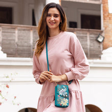 Load image into Gallery viewer, Woman in a pink outfit smiling and holding a small blue floral Anuschka genuine leather Crossbody Phone Case - 1173 with RFID card holders.
