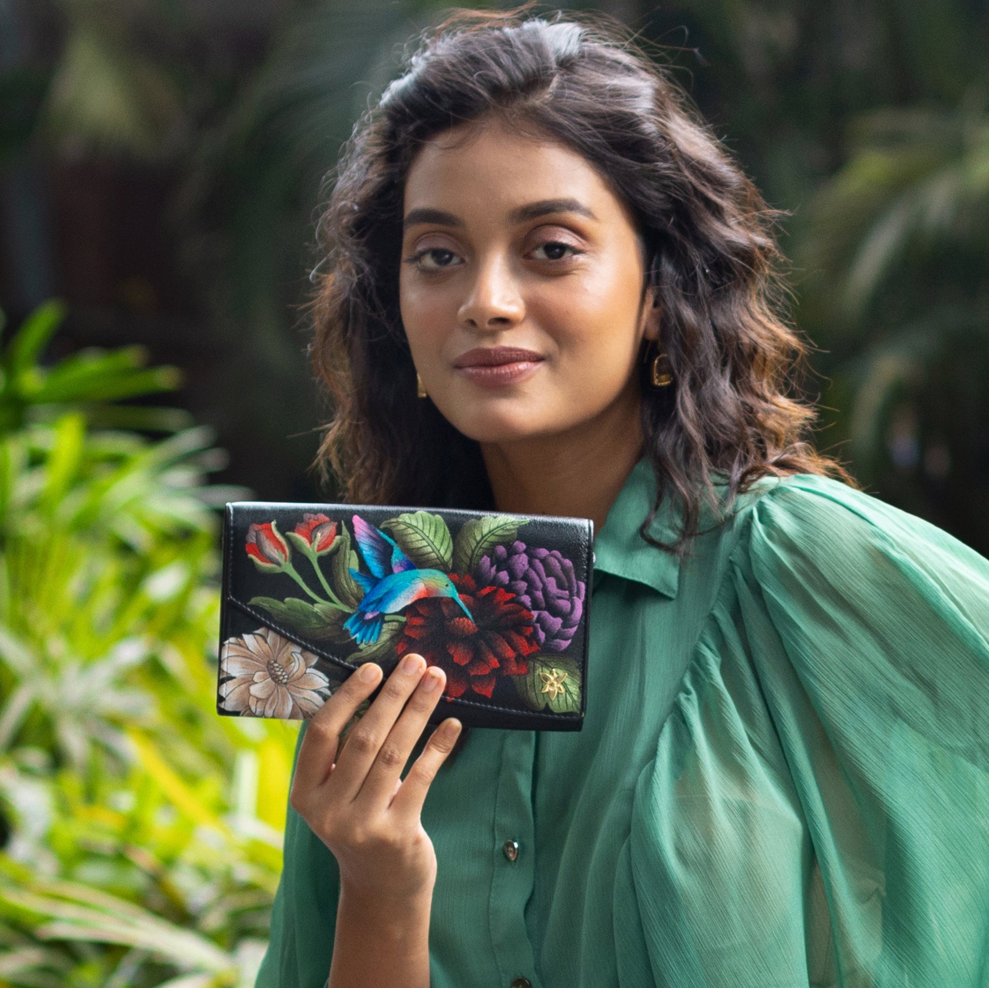 A woman holding an Anuschka Accordion Flap Wallet - 1174 with RFID protection outdoors.