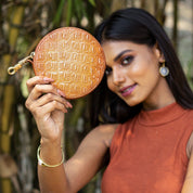 A woman holding a Round Coin Purse - 1175 from Anuschka with a focused gaze towards the camera.