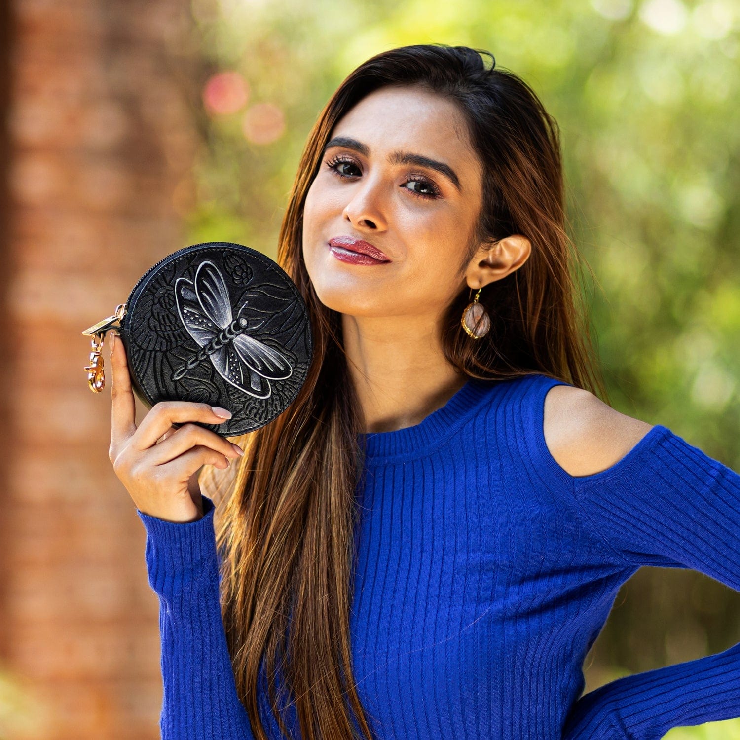 A woman in a blue top holding a Round Coin Purse - 1175 by Anuschka with a hand-painted butterfly motif.