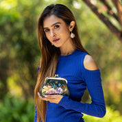 Woman in a blue dress holding a small Anuschka Clasp Pouch With Key Fobs - 1177 outdoors, radiating vintage charm.