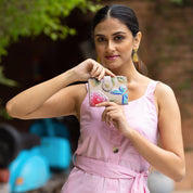 A woman in a pink dress holds a small, colorful Anuschka Two Fold Organizer Wallet - 1178 in an outdoor setting, perfectly suited for minimalists seeking a touch of charm.