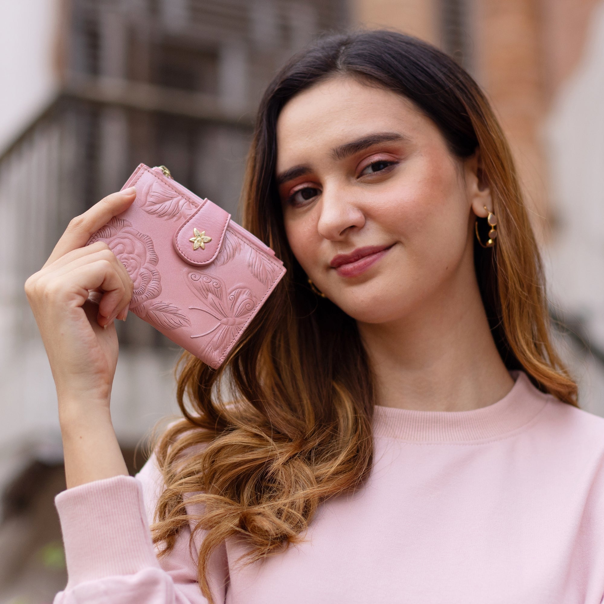 A woman holding a Anuschka Two Fold Organizer Wallet - 1178 next to her head while smiling at the camera.