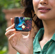 Woman holding an Anuschka Airpod Pro Case - 1179 with a hummingbird design.