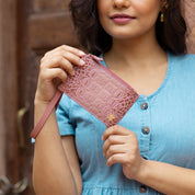 A woman holding a pink patterned Anuschka RFID clutch wristlet.