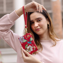 Load image into Gallery viewer, Woman holding a red floral Anuschka Card Holder with Wristlet - 1180 with RFID protection outdoors.
